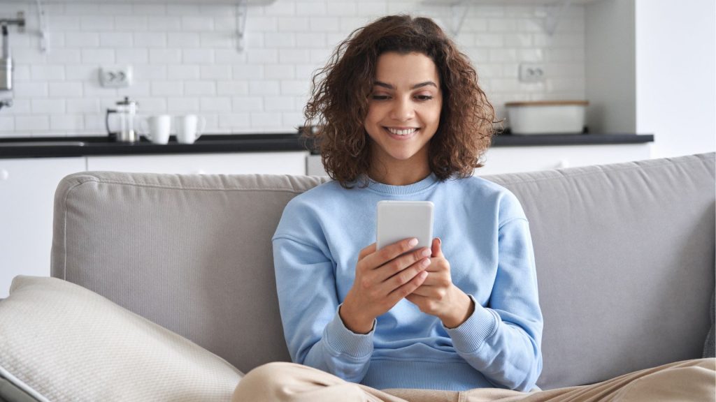Bild på en glad kvinna i en soffa som tittar på sin smartphone